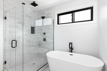 A renovated, luxury shower and freestanding bathtub with marble subway tiles, black faucet and...