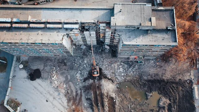 A demolition excavator destroys an old unusable building. Destruction of walls and concrete blocks. Aerial view.