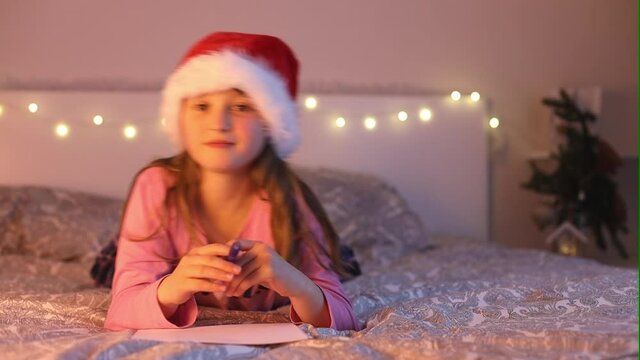 A cute girl in a sana hat writes a letter to Santa Claus for Christmas with wishes and dreams about gifts. Childhood dreams. New Year Holidays