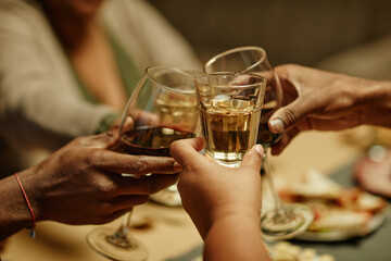 Warm toned close up of African-American family clinking glasses while enjoying dinner party at home