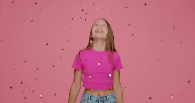 Confetti falling on happy little girl child jumping under spangles while birthday party celebration on pink background