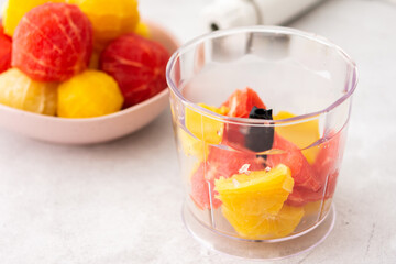 Peeled grapefruits, sweets and oranges in a plate, blender bowl with fruit, making a healthy citrus smoothie