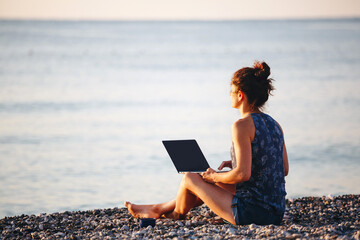 Working outdoors. Freelance concept. Technology and travel. Pretty young woman using laptop on the beach