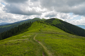 Mountain path through green grassy mountain ridge winding up in to the distant mountain peak under...