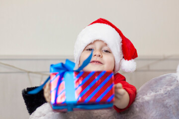 Portrait of a cute boy in a Santa Claus hat. Funny smiling child. Gifts, toys, joy, celebration.