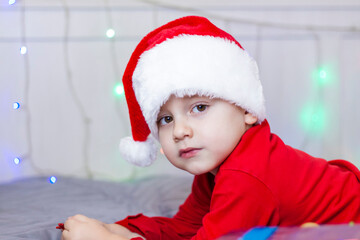 Portrait of a cute boy in a Santa Claus hat. Funny smiling child. Gifts, toys, joy, celebration.
