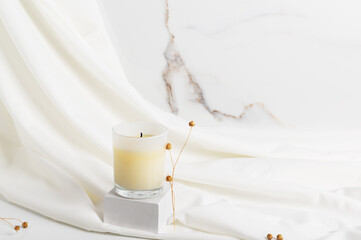 Natural wax candle on a white podium and fabric background.