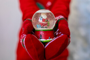 Child in Christmas pajamas holds a glass ball with snow in his hands.