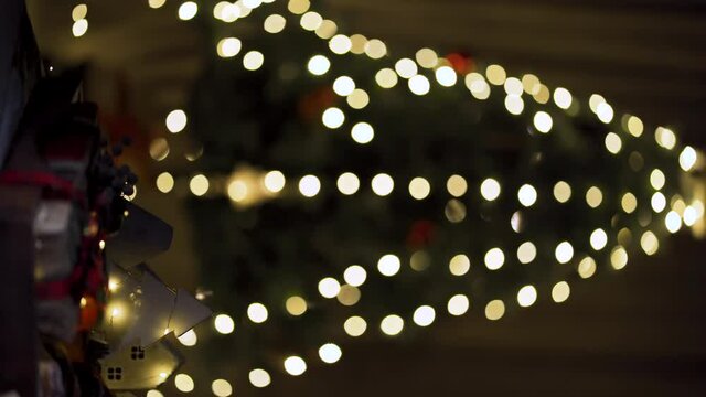 New Year gifts. A miniature decorative Christmas tree with blinking garlands. On a blurred background, lights of garlands with a Christmas tree are visible. Vertical 9x16