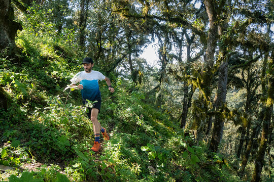 One man running on a trail surrounded by dense forest and vegetation