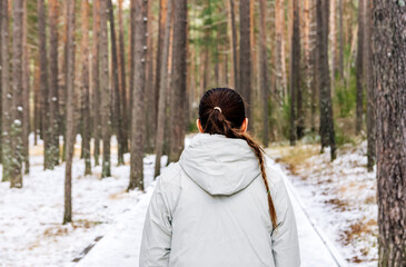 Rear view of a woman with a braid in her hair walking through a snowy forest.