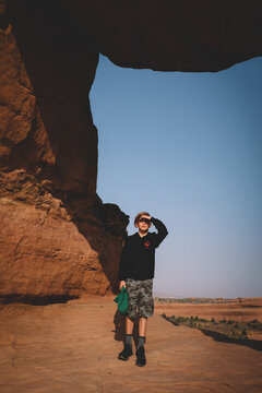 Boy Shields his Eyes from the Sun underneath a Rock Archway.