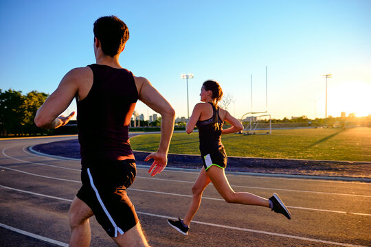 Athletes running together on track with sunset behind