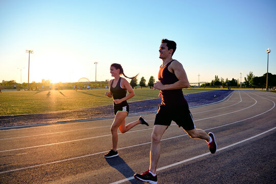 Athletes running together on track with sunset behind