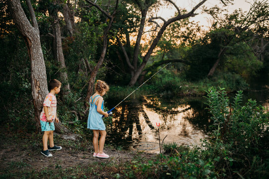 Brother and sister reeling fishing pole out of water at sunset
