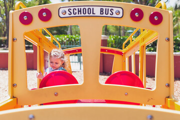 Little girl playing on a school bus toy at a playground.