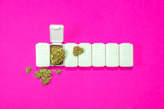 Alternative medicine concept: pillbox full of marijuana buds on pink.