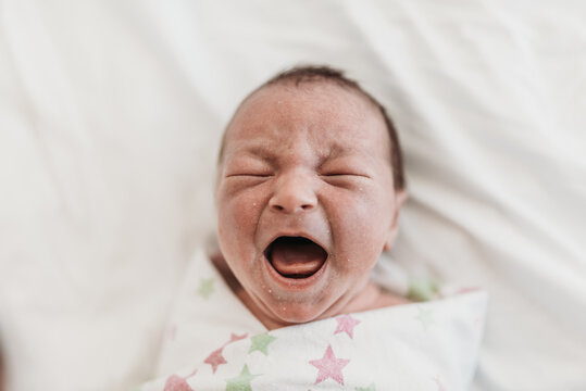 Swaddled newborn crying in hospital bed