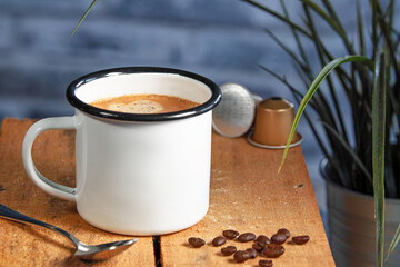 A white coffee cup with cream coffee stands on a colored wooden wooden surface