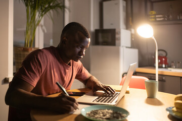 Smart black man using laptop and making notes