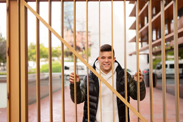 Young guy standing behind a metal fence while looking camera