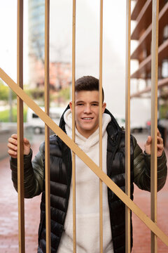 Young guy standing behind a metal fence while looking camera