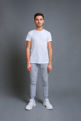 Full length portrait of confident young man in white t-shirt, isolated on gray background, vertical...