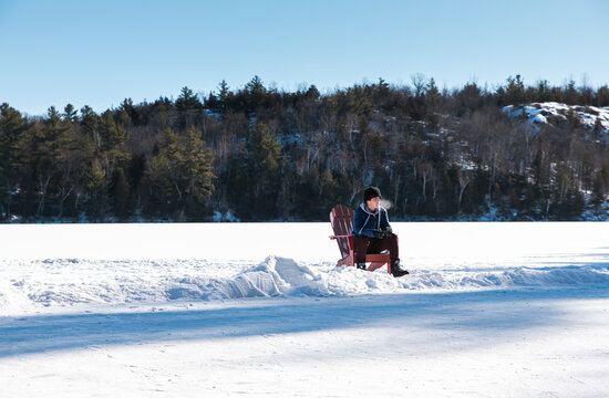 Teen boy taking a break from skating on outdoor rink on winter day.