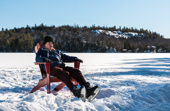 Teen boy taking a break from skating on outdoor rink on winter day.