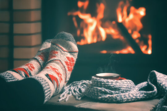 Girl resting and warming her feet by a burning fireplace in a country house on a winter evening. Selective focus.