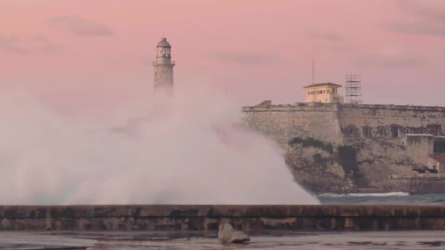 wave crashing on malecon with the Faro Castillo del Morro lighthouse. Havana, Cuba