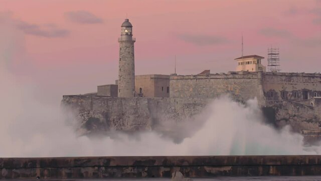 wave crashing on malecon with the Faro Castillo del Morro lighthouse.  Havana, Cuba