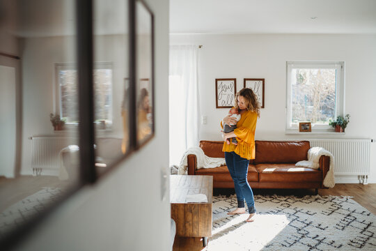 Mom holding baby standing in living room with reflection on pictures
