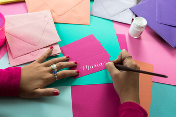 Hands of female calligrapher writing on colorful paper with white ink