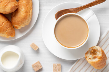 Coffee with milk in a white cup, buns and brown sugar on a white wooden table, top view, flat lay