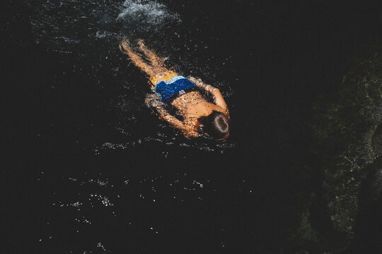 Boy in Bright Trunks Swims and Splashes in a Dark Pool