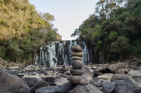 Rock Totem Made In Front Of A Beautiful Waterfall, Blurred In The Background.