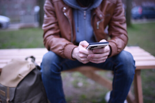 Image focused on the hands of a man with his mobile phone on a wooden bench in a park.