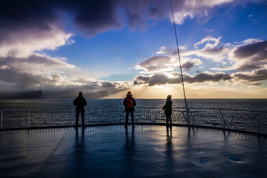 Three people enjoy the sunset on the boat deck as it leaves to Iceland