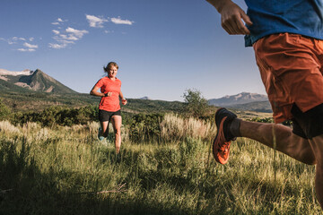 Two trail runners sprint through tall grass field with mountain view