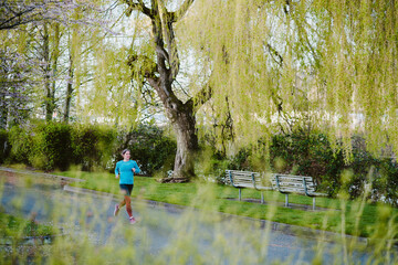 An athletic woman runs in city park surrounded by wispy green trees