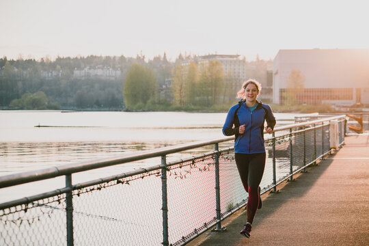 Woman run next to lake view with warm sunshine glowing behind her