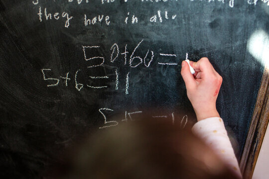 close-up of a small child writing mathematical equations on chalkboard