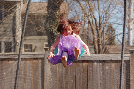 Little girl with missing teeth and colorful dress jumps on trampoline