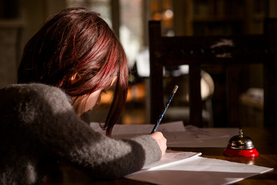 Little girl with bright red hair sits in patch of light writing story