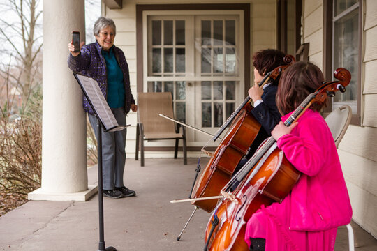 An elderly woman records two children giving cello concert on porch