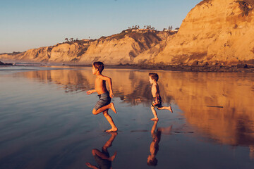 Two boys running on the beach at low tide at sunset.