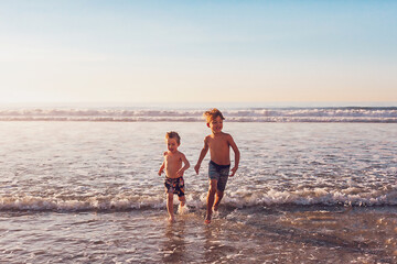 Two boys running in the water at the beach.
