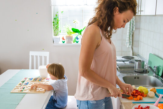 Single mother preparing healthy meal while her son playing in ba