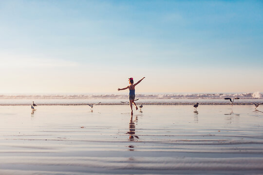 Girl running with birds at the beach at golden hour.